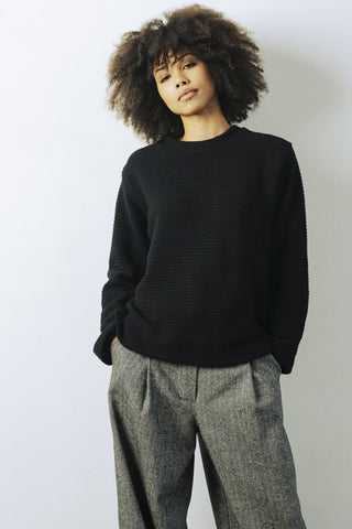 Model wearing tweed pants and black Deveron crewneck sweatshirt by Bodybag. 