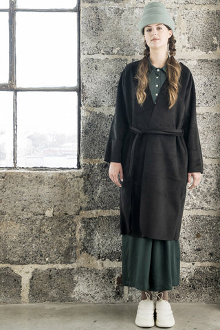 Model wearing green dress and black raw edge Inverness coat by Bodybag. 