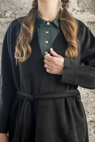 Closeup of model wearing green dress and black raw edge Inverness coat by Bodybag. 