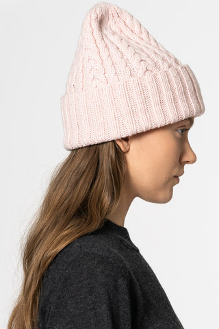 Side view of model wearing blush pink hand knit cabled merino hat by Dinadi. 