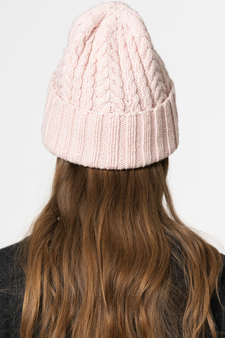 Back view of model wearing blush pink hand knit cabled merino hat by Dinadi. 