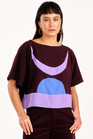 Woman wearing burgundy and lilac colour blocked Embrace top by Jennifer Glasgow. 