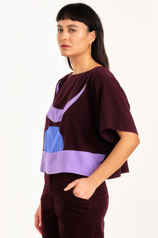 Side view of woman wearing burgundy and lilac colour blocked Embrace top by Jennifer Glasgow. 