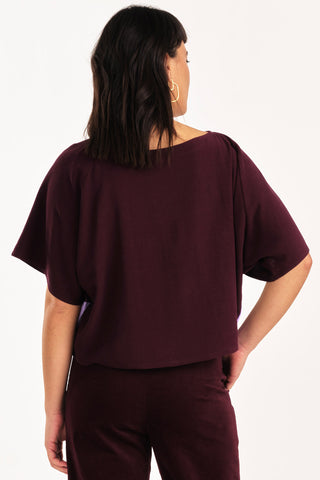 Back view of woman wearing burgundy and lilac colour blocked Embrace top by Jennifer Glasgow. 