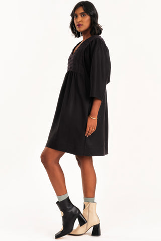 Side view of woman wearing black loose fitting empire waist Exalt dress by Jennifer Glasgow. 