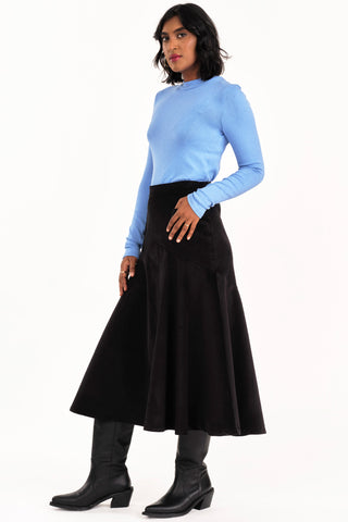 Woman wearing blue mock neck shirt and black fine corduroy flared Fjord skirt by Jennifer Glasgow. 