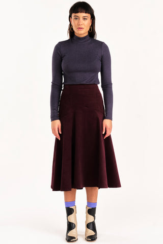 Woman wearing grey mock neck shirt and burgundy fine corduroy flared Fjord skirt by Jennifer Glasgow. 