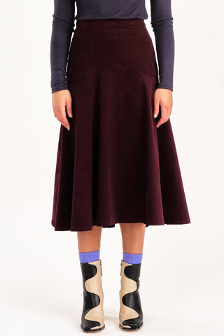 Close-up of woman wearing grey mock neck shirt and burgundy fine corduroy flared Fjord skirt by Jennifer Glasgow. 