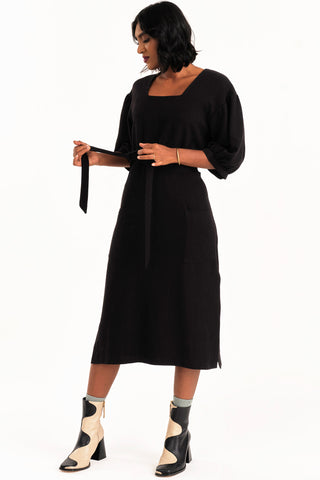 Woman dress wearing black midi length Grace dress by Jennifer Glasgow. 