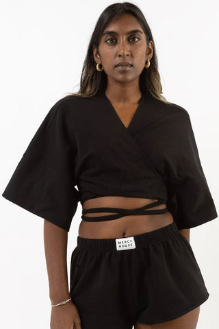 Model wearing matching black short shorts and cropped self-tie Tenbin wrap top by Mercy House. 