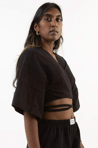 Model wearing matching black short shorts and cropped self-tie Tenbin wrap top by Mercy House. 