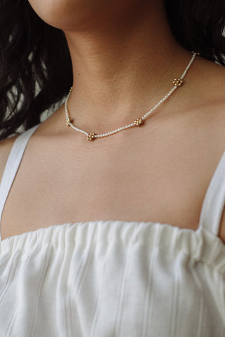 Woman wearing necklace with freshwater pearl seeds and golden beaded daisies by Kara Yoo. 