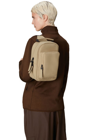 Model wearing sand coloured RAINS Book Daypack mini one strap backpack. 