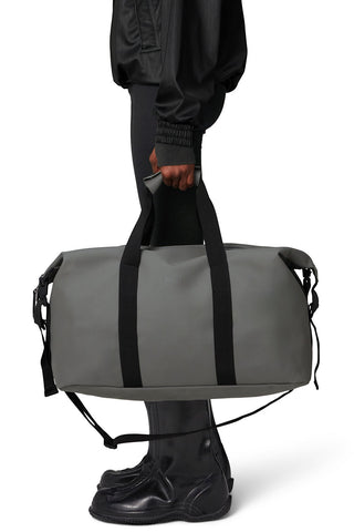 Model holding grey RAINS Hilo Weekend Bag. 