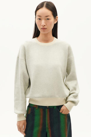 Model wearing an ecru merino wool and organic cotton Philis sweater by Thinking Mu. 