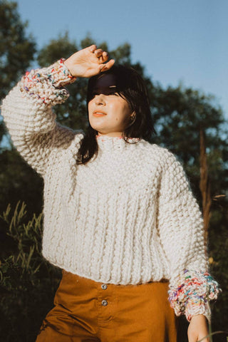 Woman covering face from sun, wearing chunky knit ivory merino wool ribbed knit Sprinkle Sweater by Toast & Yarn. 