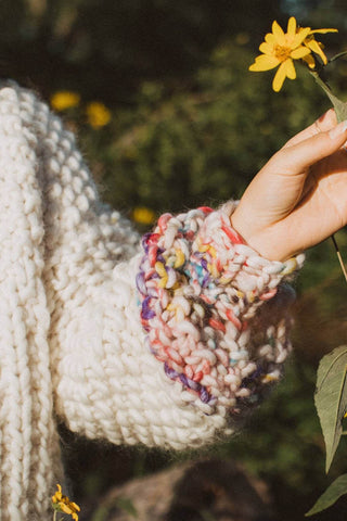 Close-up of woman holding flower and wearing chunky knit ivory merino wool ribbed knit Sprinkle Sweater by Toast & Yarn. 